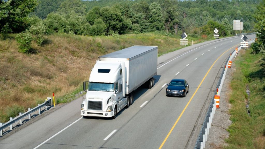 Mudanças interestaduais: caminhão em estrada com carro na pista ao lado.