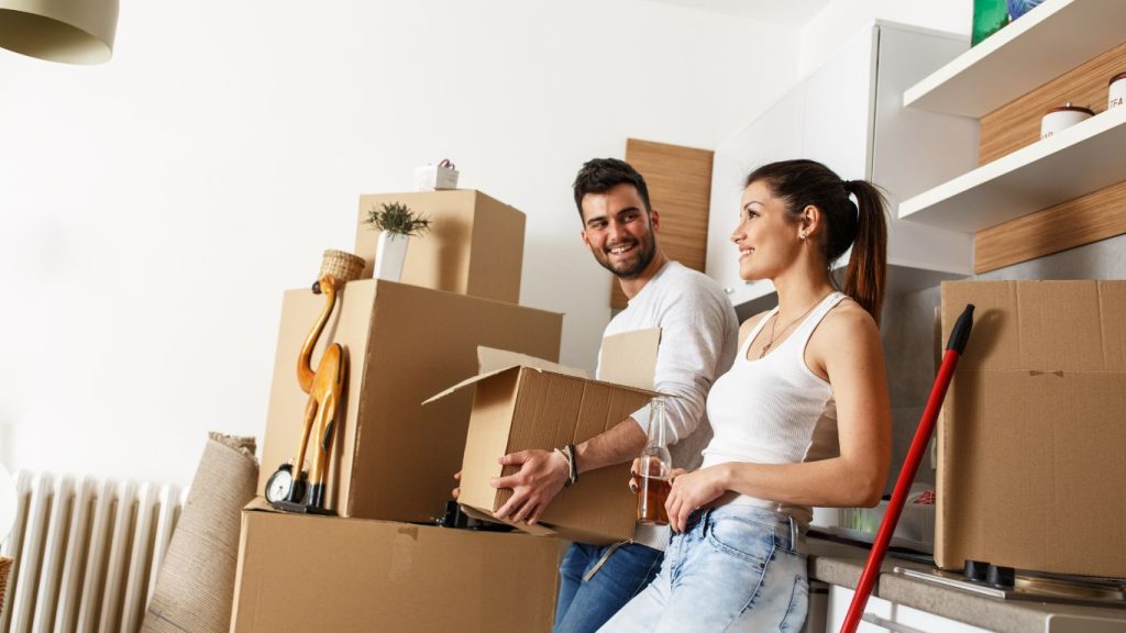 Casal em pé ao lado de caixas de papelão com mudança.